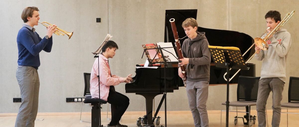 4 junge Menschen musizieren auf unterschiedlichen Instrumenten (Klavier, Trompete, Fagott und Posaune) zusammen.